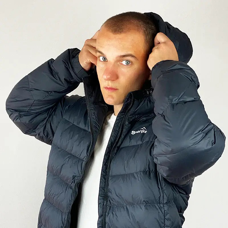 Load image into Gallery viewer, Sherpa Men's Midweight 650+ Hooded Down Jacket in black, modeled by a man adjusting the compact hood for extra warmth and comfort.