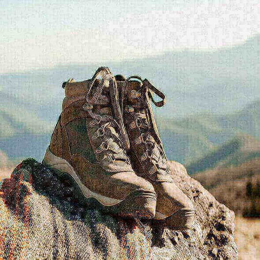 A pair of sturdy hiking boots on a rock with mountains in the background, highlighting the essential characteristics of good hiking shoes.