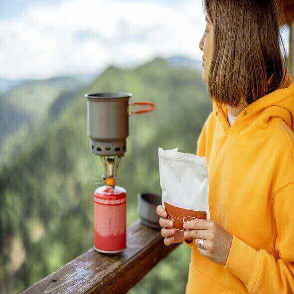 Woman preparing eco-friendly hiking meal with portable stove in scenic outdoor setting