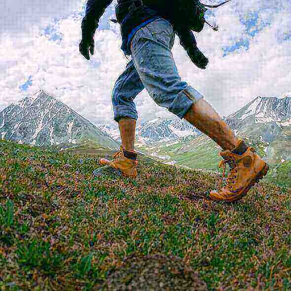 Man hiking in rugged terrain wearing durable hiking boots with scenic mountain backdrop.