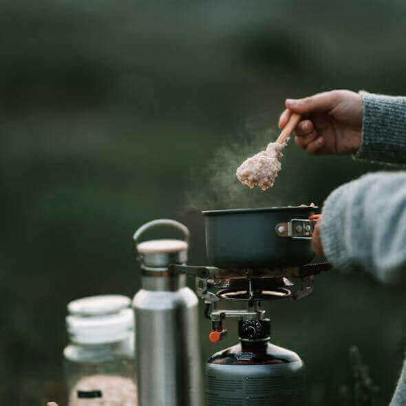 Cooking sustainable camping cuisine on a portable stove during an outdoor adventure.