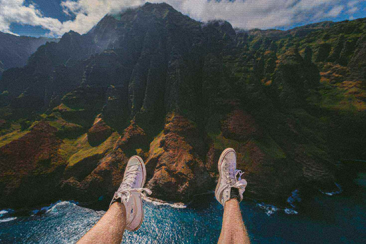 Traveler's feet in sneakers dangling over a scenic mountain landscape during an adventure trip.