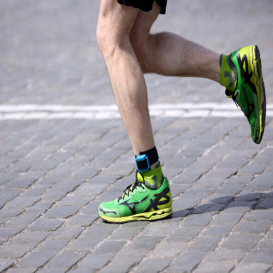 Runner wearing vibrant green and yellow barefoot shoes on a cobblestone path, showcasing natural movement.