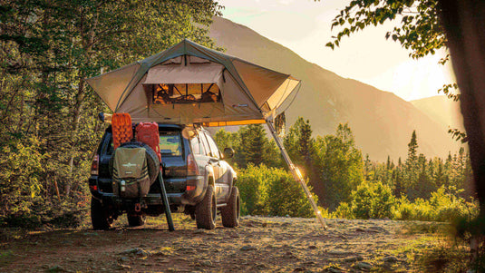 SUV with roof tent set up in a scenic forested camping spot with mountain view at sunset. - Adventureco Blog