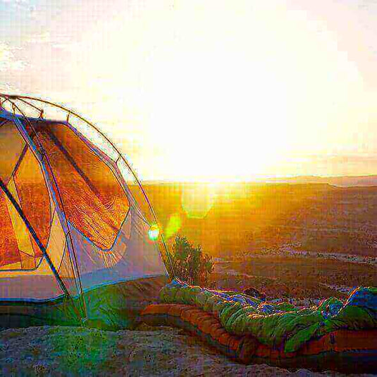 Tent and sleeping bags set up on a hilltop at sunrise, illustrating outdoor adventure and durability tips for extending a sleeping bag's lifespan. - Adventureco Blog