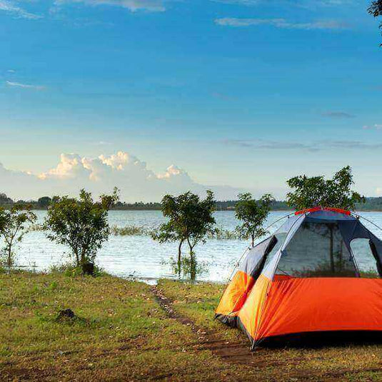 Orange tent set up by a serene lakeside under a clear blue sky, ideal for sustainable camping adventures.