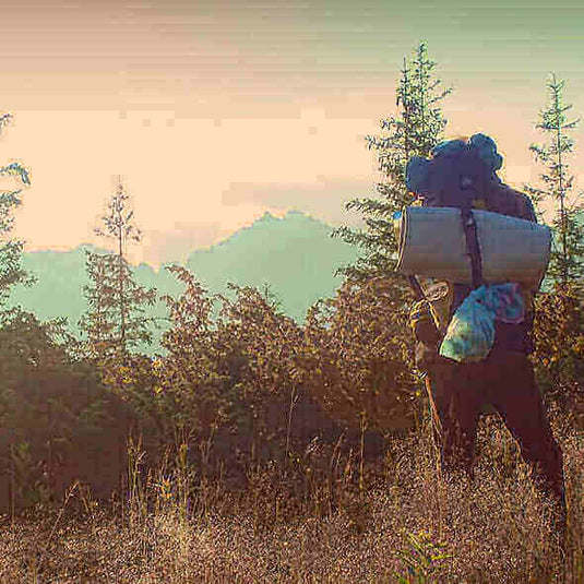 Person hiking with camping gear essentials in a forest at sunset