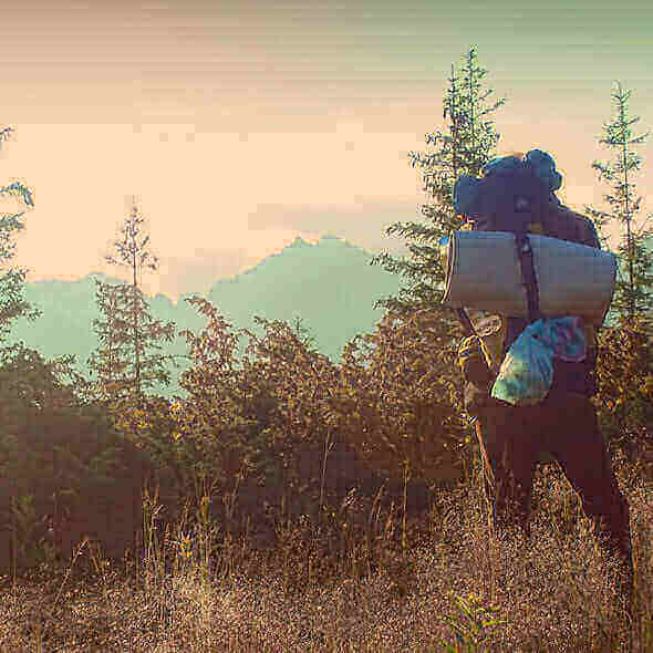 Person hiking with camping gear essentials in a forest at sunset