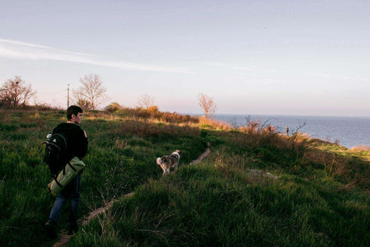 Man hiking on a coastal trail with his dog, preparing for a camping trip. - Adventureco Blog