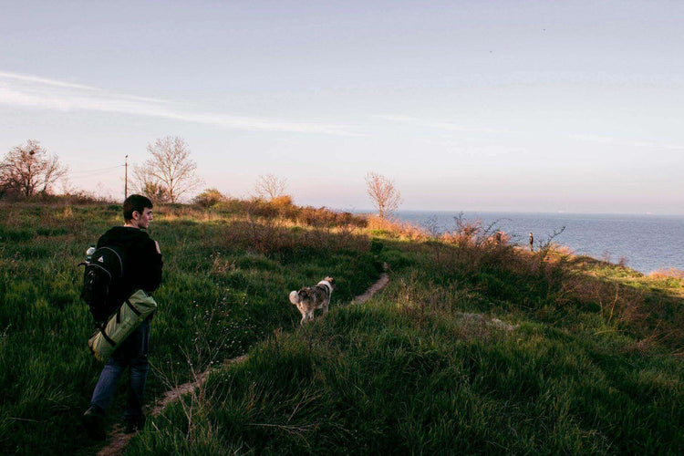 Man hiking on a coastal trail with his dog, preparing for a camping trip.