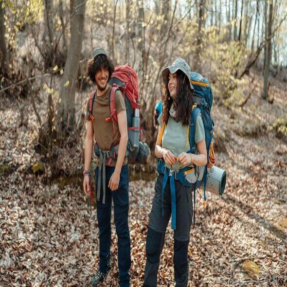 Two hikers wearing eco-friendly hiking clothes with backpacks, standing in a forest trail during a sunny day.