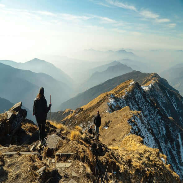 Hikers exploring a mountain trail with stunning panoramic views of layered hills and valleys.