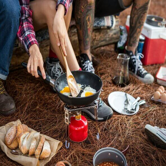 Preparing a delicious meal while camping, frying eggs over a portable stove in a forest setting.