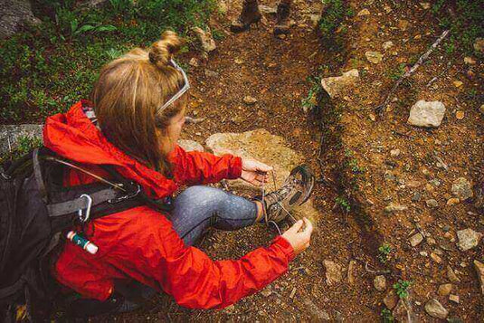 Woman wearing Vivobarefoot shoes ties her laces while hiking in the woods.