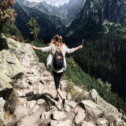 Woman hiking on rocky trail in Australia's mountainous landscape with backpack and trekking pole