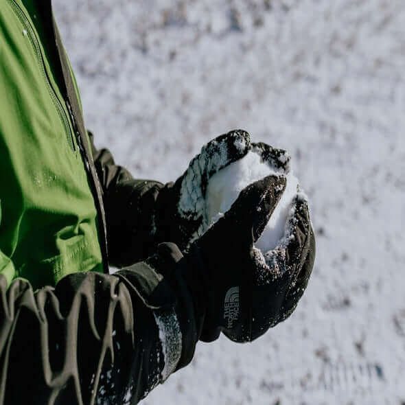 Person wearing gloves holding a snowball in a winter landscape.