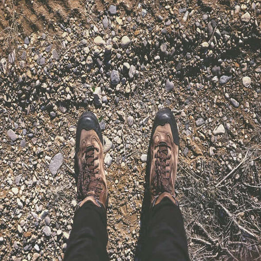 A pair of minimalist hiking boots on a rocky outdoor trail, highlighting their design for natural foot movement.