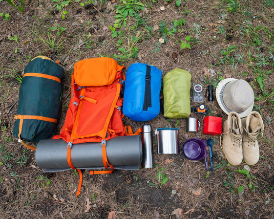 Sustainable camping gear on forest ground, featuring eco-friendly tents, hiking boots, a reusable water bottle, and a backpack.