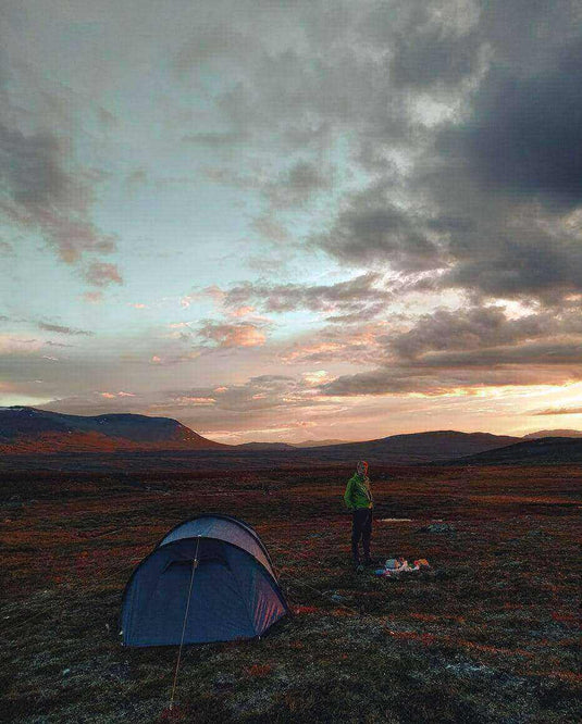 Camper standing near a tent at sunset, demonstrating how to manage tent condensation during a camping trip.