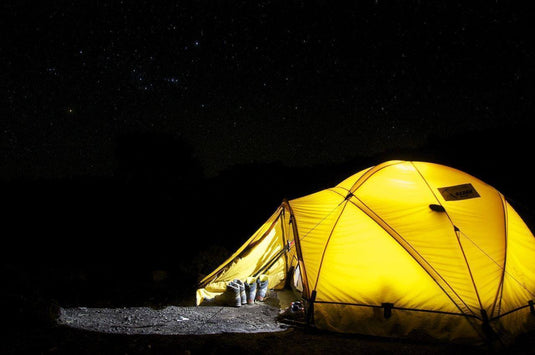 Bright yellow camping tent illuminated at night with a starry sky, demonstrating tarp effectiveness in outdoor settings. - Adventureco Blog