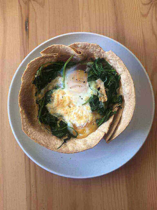 Spicy Mexican breakfast bowl with egg, spinach, and tortilla on a white plate and wooden table.
