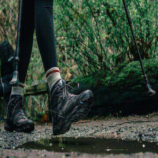 Close-up of hiker wearing waterproof hiking boots while walking on a trail with walking sticks.