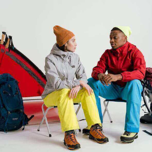 Two people in outdoor gear discussing sustainable practices in the outdoor gear industry, seated near camping equipment.