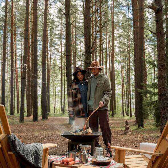 Couple enjoying a sustainable outdoor adventure in the forest, cooking over a campfire for an eco-friendly camping experience.