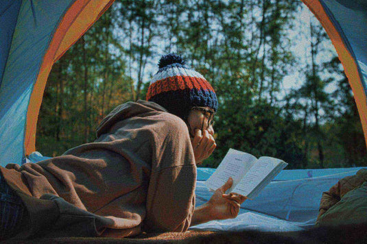 Camper reading a book on a sleeping pad inside a tent in the outdoors