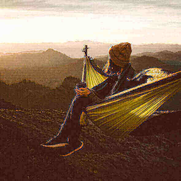 Person in a yellow hammock enjoying a mountainous sunset during a hammock camping trip.