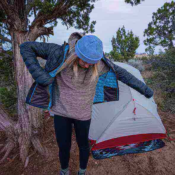 Hiker layering clothes for comfort and style near a tent in the outdoors