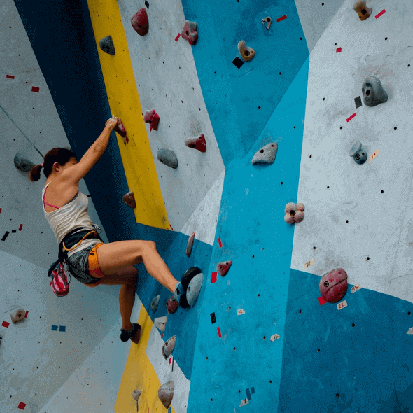 Woman rock climbing indoors with proper climbing gear and tools to stay injury-free