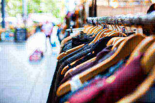 Clothing rack with various garments hanging on wooden hangers at an outdoor market.