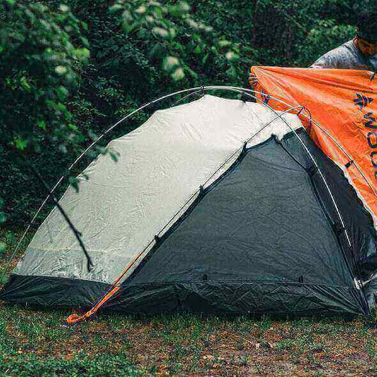 Camper assembling a double-layered tent amidst lush greenery in Queensland, preparing for a summer storm while camping.