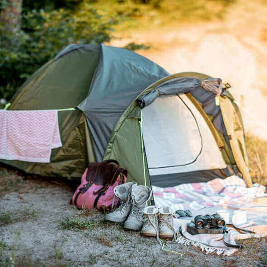 Vegan and eco-friendly camping gear including a tent, hammock, boots, and binoculars set up in the great outdoors - Adventureco Blog