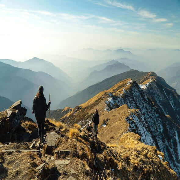 Hikers exploring a mountain trail with stunning panoramic views of layered hills and valleys.
