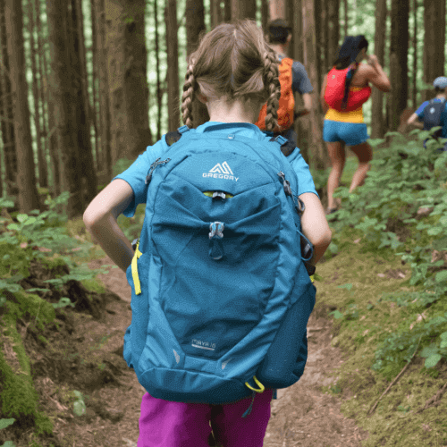 Child hiking on a forest trail wearing blue backpack and warm clothing, ideal gear for kids' outdoor adventures.