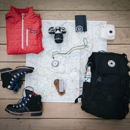 Camping gear including a jacket, compass, boots, backpack, cameras, and a map laid out for an eco-friendly adventure. - Adventureco Blog