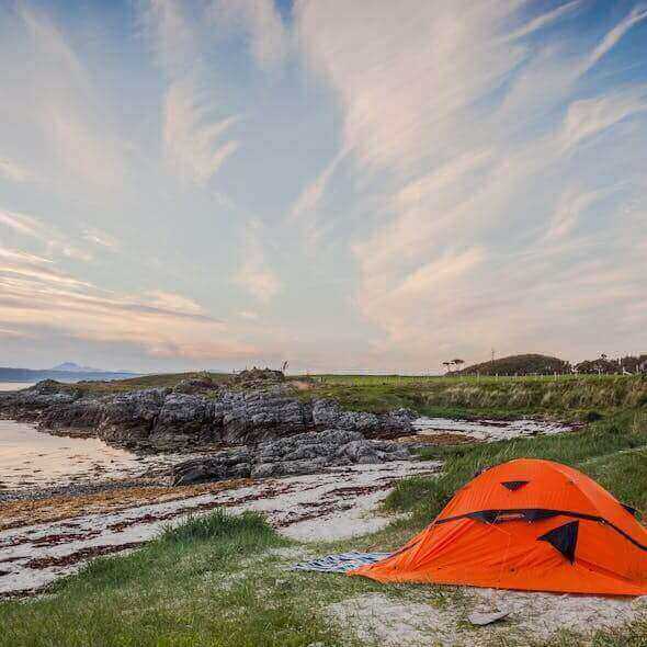 Zero-waste camping setup with orange tent by scenic Australian coastline at sunset