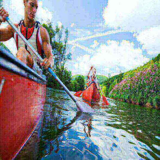 Canoeing on a calm river with vibrant greenery and a clear sky, promoting outdoor activities to reduce stress.