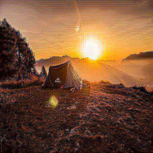 Tent pitched on a hilltop with a beautiful sunrise background and mountain views, perfect for a camping trip.