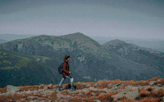 Hiker in autumn outfit walking on rocky mountain trail with backpack