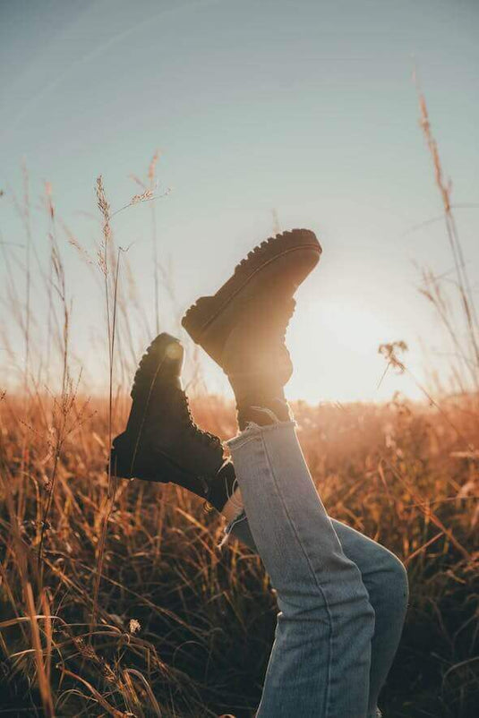 Person wearing black Doc Martens boots in a sunlit grassy field, showcasing outdoor adventure style. - Adventureco Blog