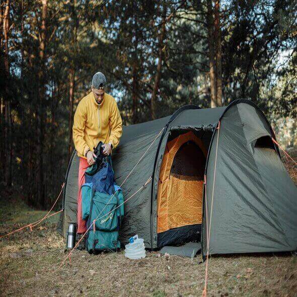 Camper setting up colorful camping gear beside a green tent in a serene forest to enhance the outdoor experience