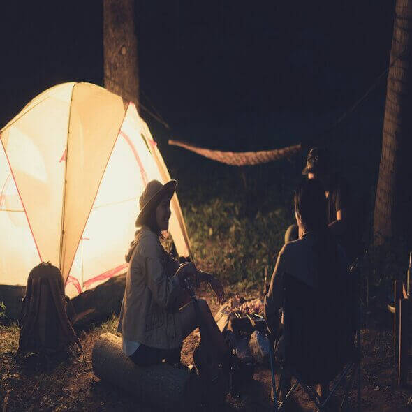 Camping group enjoying energy-efficient lantern light near tent at night in forest setting.