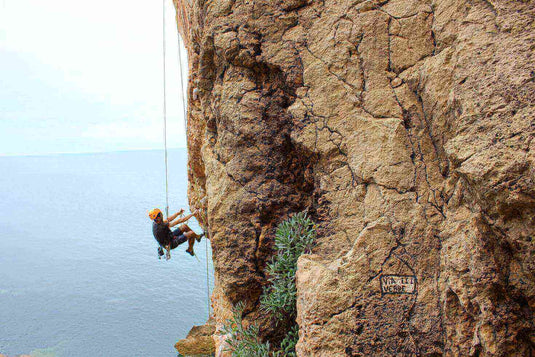 Person rock climbing with a harness on a rugged cliff face overlooking the sea