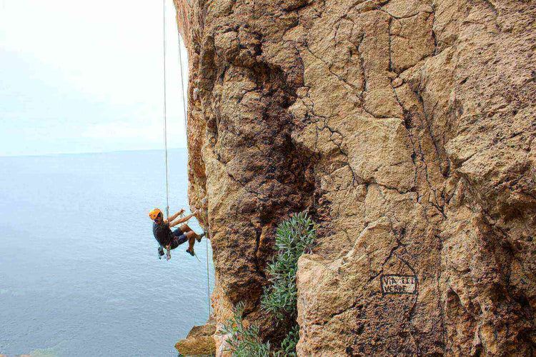 Person rock climbing with a harness on a rugged cliff face overlooking the sea