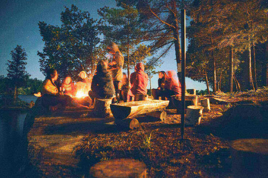 Group of campers gathered around a campfire at night in a forest setting, practicing sustainable camping.