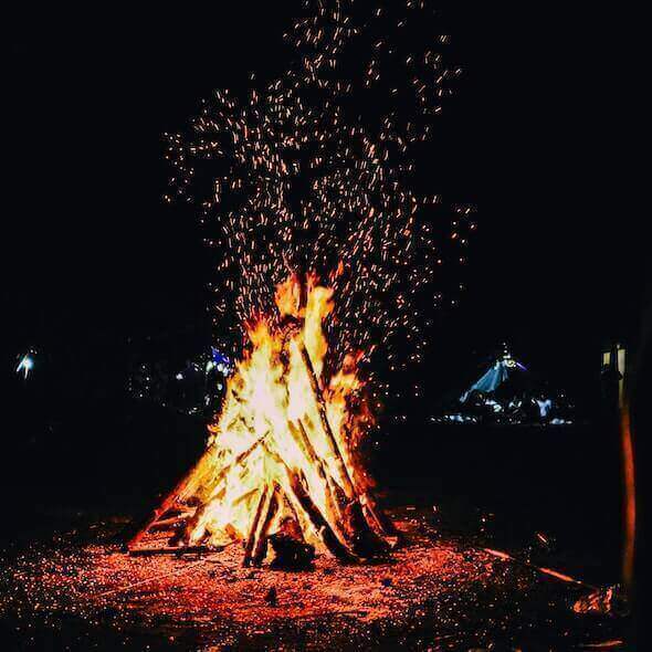 Campfire burning brightly in the Australian Outback at night, illuminating the campsite with sparks flying into the sky.