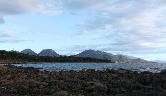 Scenic view of Glass House Mountains in Australia's mountaineering adventure destination, featuring rocky shoreline and lush greenery - Adventureco Blog